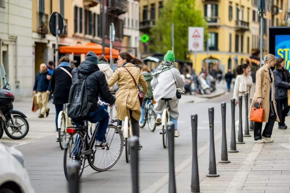 People on bikes and pedestrians walking on busy city street in Milan, Italy